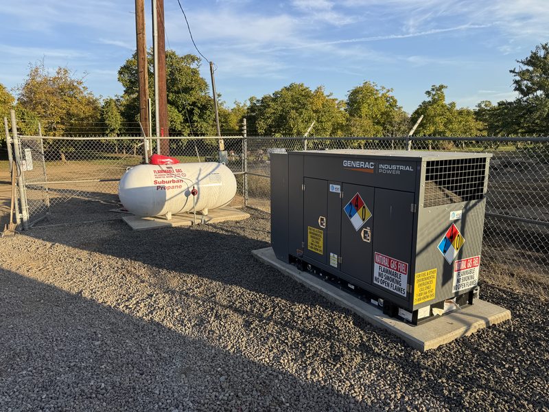 Generac industrial generator beside propane tank at a fenced site at golden hour