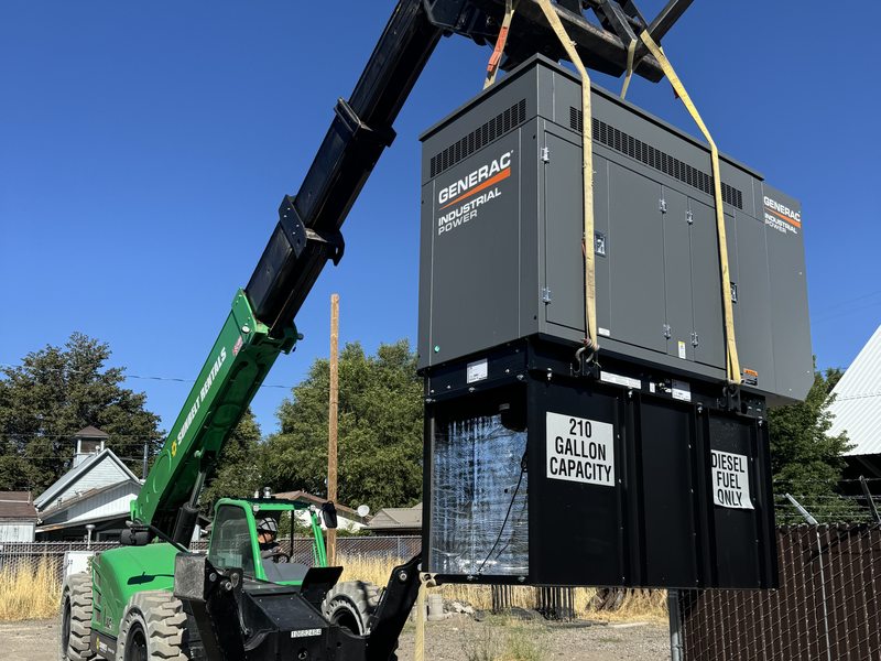 Telehandler lifting a Generac industrial generator with 210-gallon base tank into position