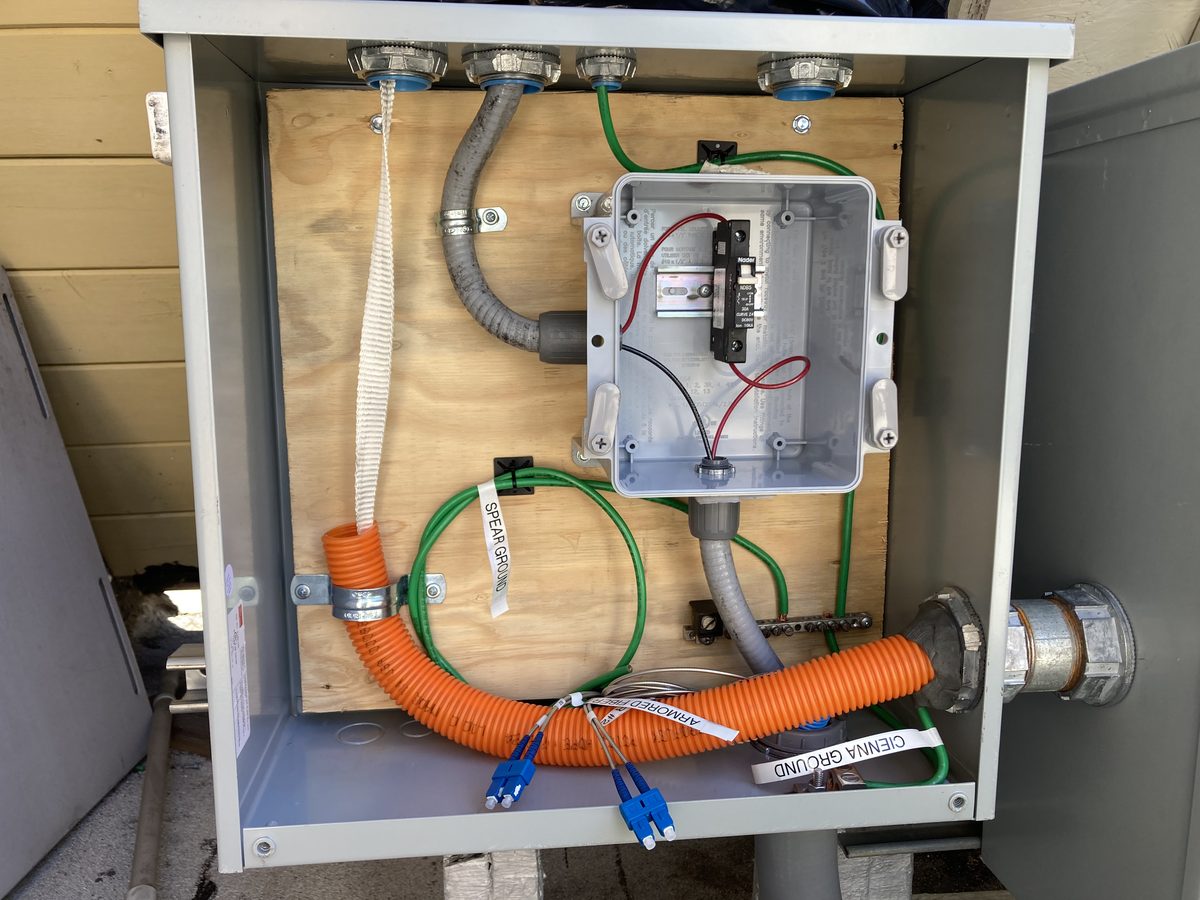 Open cabinet with armored fiber, labeled spear and antenna grounds, and breaker