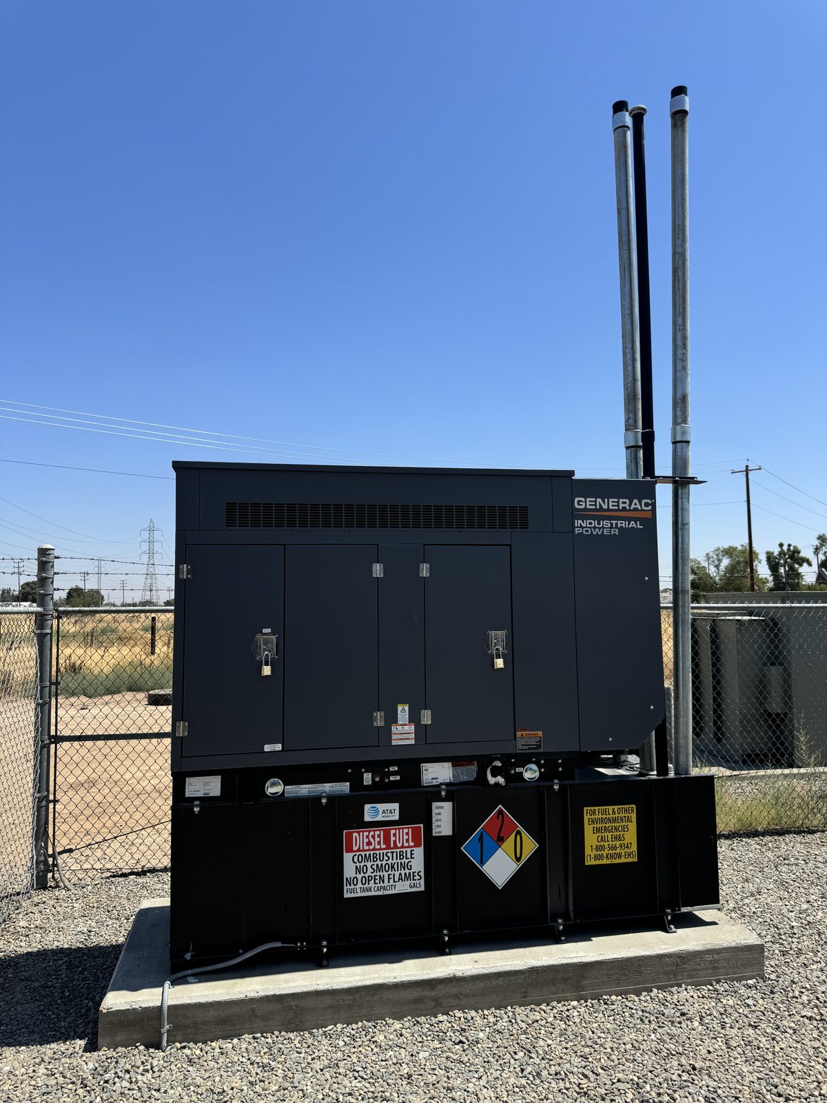 Diesel standby generator with dual exhaust stacks on concrete pad at a fenced site
